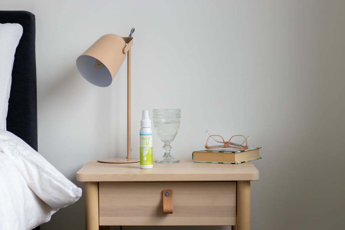 FunghiClear® nagelspray op een nachtkastje, waarmee wordt getoond hoe gemakkelijk het in een dagelijkse routine voor de behandeling van schimmelnagels past.
