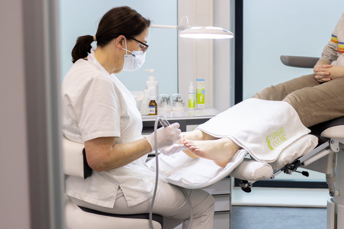 Een voetverzorgingsspecialist voert een voetbehandeling uit bij een patiënt met een schimmelinfectie aan de teennagels in een kliniek. De voetverzorgingsspecialist gebruikt FunghiClear om de schimmel te bestrijden.
